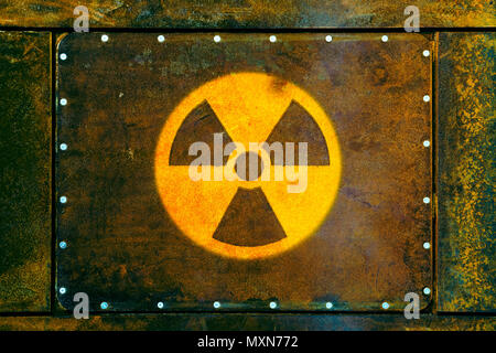 Round yellow radioactive (ionizing radiation) danger warning symbol painted on a massive rusty metal plate fixed with metallic screws to the wall and  Stock Photo