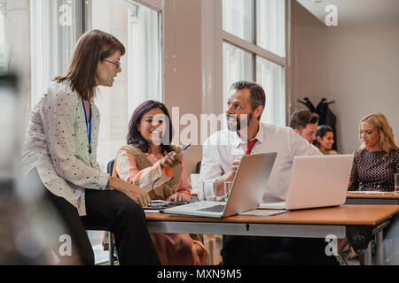 Co-workers talking though information on a laptop in a board room. Having a meeting in the conference. Stock Photo
