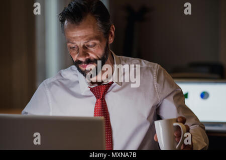 Front view of a businessman working late in the office to get his work finished before the deadline. Stock Photo