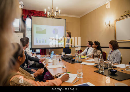 Point of view angle of a ground of business people sitting around a table looking at a businesswoman giving a presentation. Stock Photo