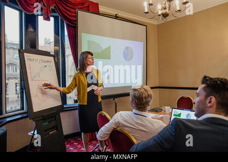 Side view of a businesswoman pointing at a flip chart with graphs and charts on. Having a staff meeting and talking about finances. Stock Photo