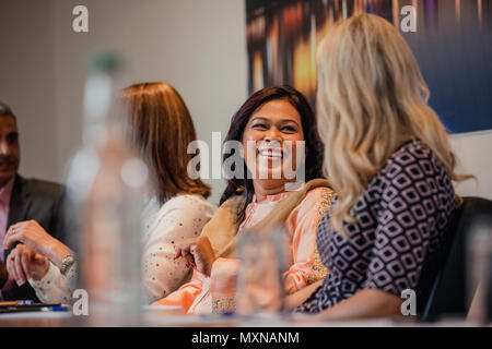 Two businesswomen talking while sitting down at a conference table. Waiting for the meeting to start. Stock Photo