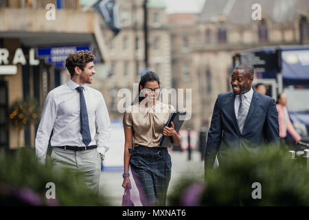 Front view of three business people walking through the city streets. All three people are wearing formal clothing. Stock Photo