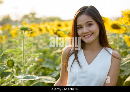 Young happy beautiful Asian woman smiling in the field of bloomi Stock Photo