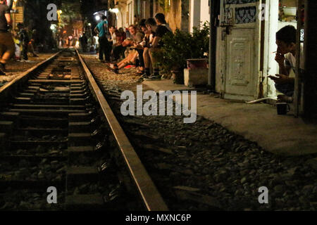 Hanoi, Vietnam - March 14, 2018: People sitting in Train street, one of the most recognizable touristic landmarks, at night. Stock Photo