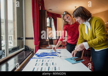 Two businesswomen looking for their name badges on the table before the conference starts. Stock Photo