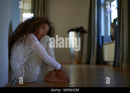 A young preteen mixed race girl with big curly hair sitting on the floor in her bedroom looking sad and upset Stock Photo