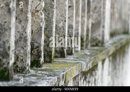 Stone fence with parallel concrete poles and old green moss. Stock Photo