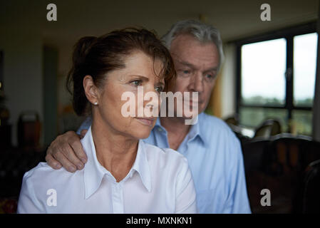 Elderly couple together art home, the husband is seen comforting his wife in a loving embrace after receiving some bad news Stock Photo