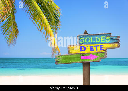 Soldes d'ete (meaning summer sale in French) written on pastel colored wooden direction signs, beach and palm tree background Stock Photo