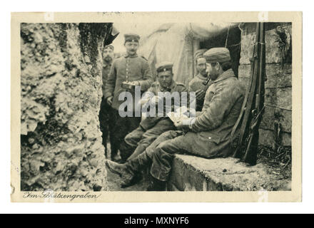 German historical photo postcard:  Soldiers in the trench Smoking pipes, playing cards. One holds a frying pan with food. In between attacks. wwi Stock Photo