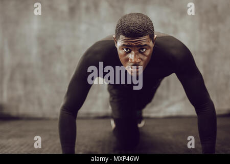 Athletic man doing push up exercise in the gym. Muscular man in tight black outfit doing crossfit training. Stock Photo