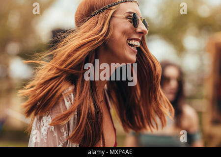 Laughing young woman in retro look at music festival. Pretty young woman smiling in sunglasses at park. Stock Photo