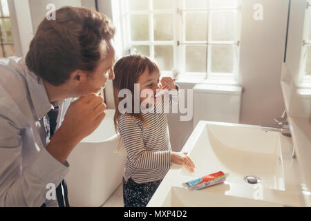 Father and daughter brushing teeth standing in bathroom. Man teaching his daughter how to brush teeth. Stock Photo