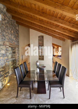 dining room interior in the foreground the glass dining table with brown leather chairs the floor and the wall are made of stone while the ceiling is  Stock Photo