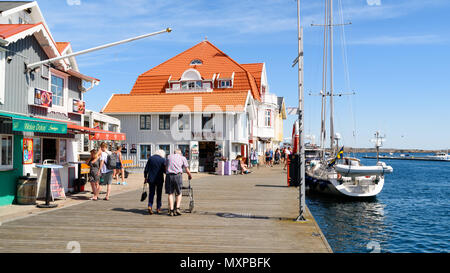 Smogen, Sweden - May 19, 2018: Travel documentary of everyday life and place. Tourists spending a day at the pier in the village. Boats moored just be Stock Photo