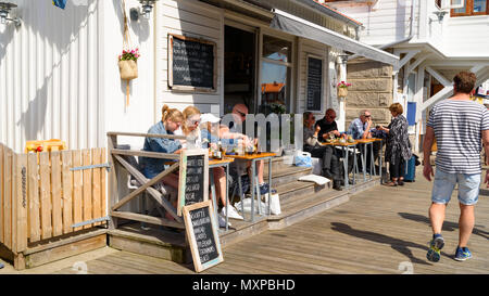Smogen, Sweden - May 19, 2018: Travel documentary of everyday life and place. Tourists sitting at an outdoor diner eating while looking at passing peo Stock Photo