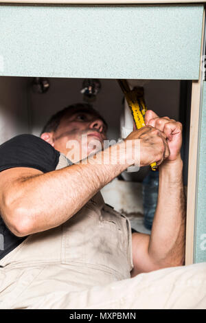specialist male plumber repairs faucet in kitchen Stock Photo