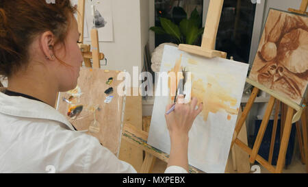 Young female artist in apron painting with oil on white canvas Stock Photo