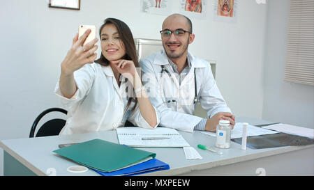 Young doctor and pretty nurse taking selfies on the phone at their desk Stock Photo