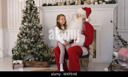 Cute little girl singing a Christmas song sitting on Santa Claus lap Stock Photo