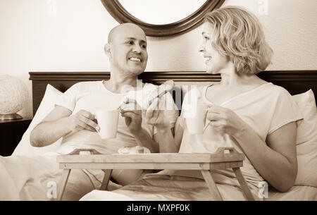 Joyful smiling mature spouses enjoying breakfast in bed in the morning Stock Photo