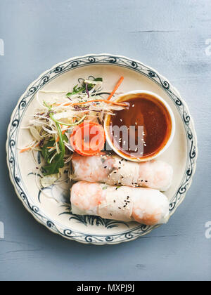 Asian style dinner. Flat-lay of steamed dumplings Dim sum and summer rice paper rolls with shrimp and sauce over blue table, top view, copy space. Chinese cuisine Stock Photo