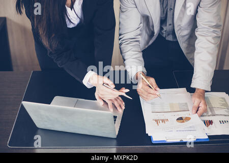 Asian businesswomen holding a pen and analysis documents on office table with laptop computer and graph financial diagram working in the background Stock Photo