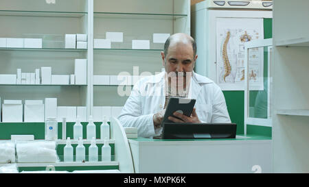 Senior pharmacist with mustache working on tablet pc checking medicine in pharmacy Stock Photo