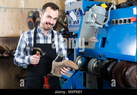 Smiling english male worker fixing failed shoes in shoe repair workshop Stock Photo