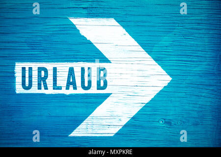 Urlaub (in German language, Holiday or Vacation) text sign written on a white directional arrow on a blue wooden signboard. Concept for tropical beach Stock Photo