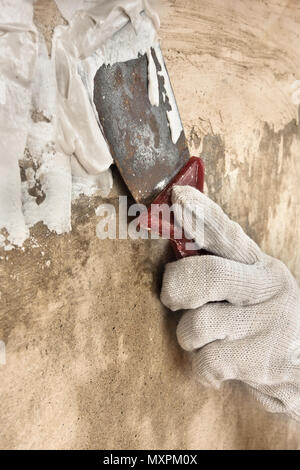hand in glove plastering concrete wall with putty knife during repair Stock Photo