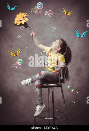 Studio shooting in retro style. A girl with a sunflower in her hand on a blue background catches butterflies and soap bubbles. Stock Photo