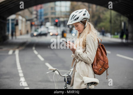 Young businesswoman checking the notifications on her mobile phone while cycling to work. Stock Photo