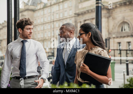 Side view of three business people walking towards the front of a hotel for a business meeting. Stock Photo