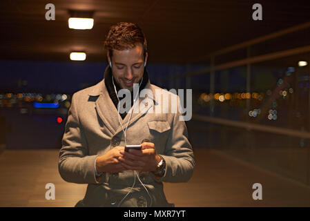 Businessman wearing a winter coat in early morning darkness walking through the city talking on his mobile phone through ear buds Stock Photo