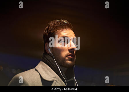 Businessman wearing a winter coat in early morning darkness walking through the city talking on his mobile phone through ear buds Stock Photo