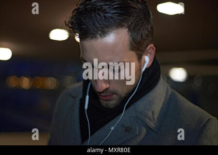 Businessman wearing a winter coat in early morning darkness walking through the city talking on his mobile phone through ear buds Stock Photo