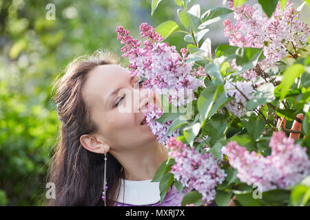 Young pretty woman with nice earrings smelling a blooming lilac flowers Stock Photo