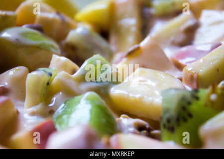 Plate with chopped apples and kiwis mixed with granola and yogurt. A steel spoon rest in the fruit. Stock Photo