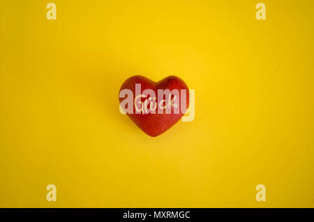 Red painted pebble in the shape of the heart on yellow background. 'Gluck' in german, luck translated in english is the message written on it. Stock Photo