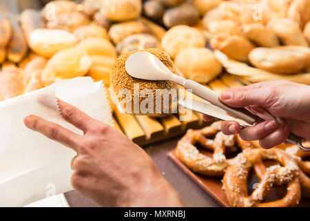 Sales woman in baker shop putting bread roll in paper bag Stock Photo