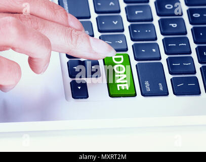 Closeup of crop finger pressing green button with word Done on laptop keyboard Stock Photo