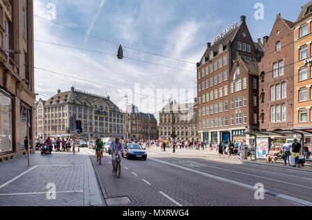 AMSTERDAM, NETHERLANDS - MAY 27: (EDITORS NOTE: Image has been digitally enhanced.) People bike and walk at the intersection of the Damrak Street and Dam Square on May 27, 2018 in Amsterdam, Netherlands. The first day's task of many tourists is to walk through the Damrak Street to the Dam Square. Stock Photo