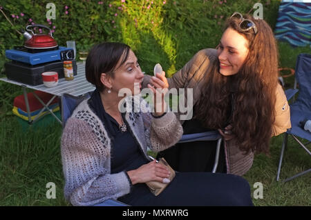 A daughter applies make-up to her mother on a campsite. Stock Photo