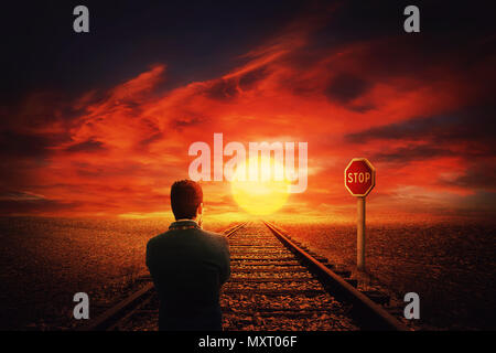 Surreal view as a man walking on a railroad along desert in front of a STOP road sign. Beautiful sunset background and businessman thinking his next m Stock Photo