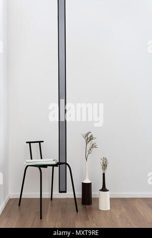 Room in a modern style with white walls and a parquet on the floor. There is a fancy long lamp on the wall. Next to it there is a chair with books and Stock Photo