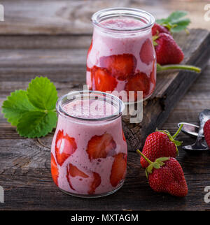 yogurt with fresh red strawberries in a glass jar on a gray wooden table, close up Stock Photo