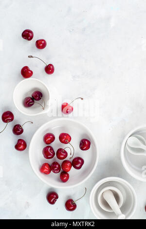 Minimalist cooking concept with red cherries and porcelain baking dishes on a white stone background. White on white flat lay with copy space.