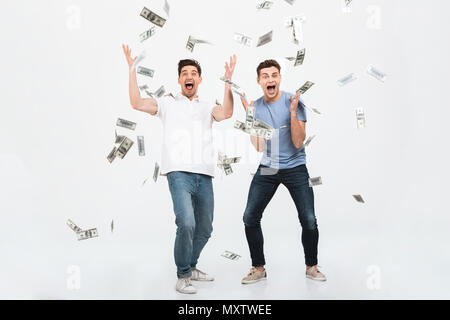 Full length portrait of two happy young men standing under money banknotes shower and celebrating success isolated over white background Stock Photo